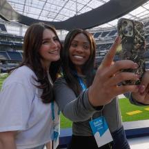 two women holding up a snake cell phone at a stadium