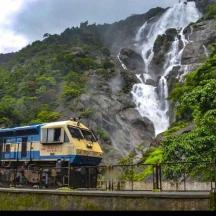 a blue and yellow train on the tracks near a waterfall