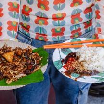 a person is holding two plates of food with chopsticks