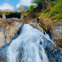 una cascada en un penya-segat amb un pont al fons
