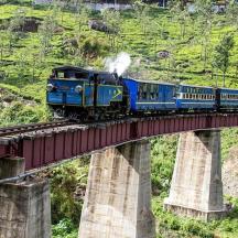 a blue train on a bridge over a mountain
