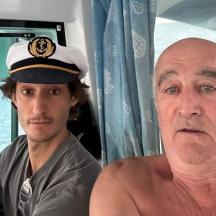 un uomo a torso nudo seduto accanto a un uomo che indossa un cappello da marinaio