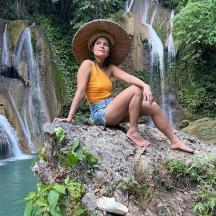 una dona asseguda en una roca davant d'una cascada
