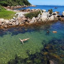 a person swimming in the water near a rocky beach