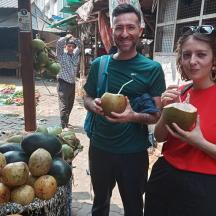 a man and a woman holding coconuts in front of a fruit stand
