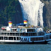 a ferry boat in the water in front of a waterfall
