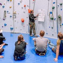 a group of people sitting in front of a climbing wall