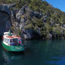 a green and white boat in the water next to a mountain