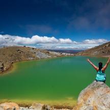 a woman standing on a rock in front of a green lake