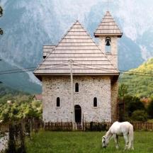 ein weißes Pferd grast auf einem Feld neben einem Gebäude
