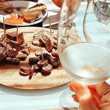 osoba koja drži čašu vina pored tanjura s hranom