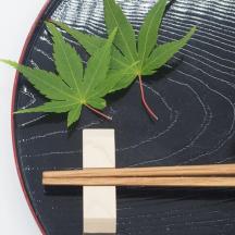 a green leaf on top of a black plate with chopsticks