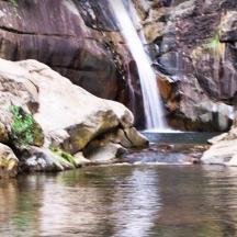 ein Wasserfall in einem Wasserbecken neben einem Fluss