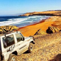 a white truck parked on a beach with a surfboard on top