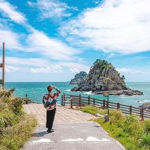 a woman standing on a path looking at the ocean