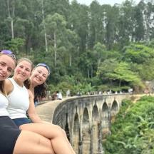 three girls sitting on a wall near a bridge