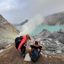 two people on a mountain looking at a geyser