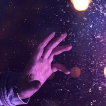 a persons hand reaching up into the air with lights in the background