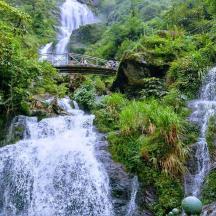 a waterfall with a bridge in front of a mountain
