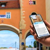 oseba, ki drži mobilni telefon pred stavbo