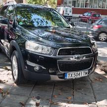 a black car parked on a sidewalk next to a tree