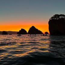 una posta de sol sobre l'aigua amb roques a l'oceà