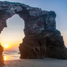 gerbang di dalam batu di pantai dengan matahari terbenam