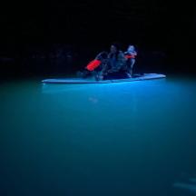 two people sitting on a snowboard in the water at night