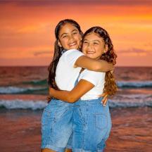 two girls hugging on the beach at sunset