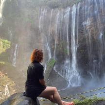 una dona asseguda en una roca davant d'una cascada