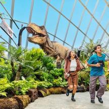 a group of people walking in front of a dinosaur statue