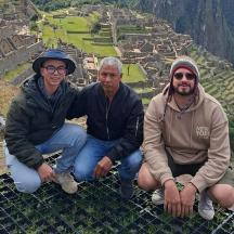 three men sitting on the edge of a pyramid at the incan ruins