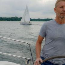 un uomo in piedi sulla prua di una barca con una barca a vela