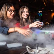 two women standing next to a table with smoke