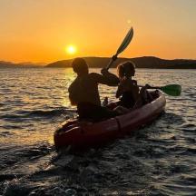 a man and a woman in a canoe on the water at sunset