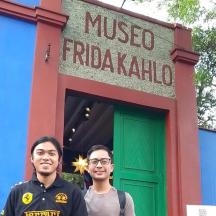 Dos hombres de pie frente a un cartel de Frida Kahlo.