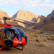 a red helicopter parked next to a river in a canyon