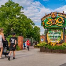 two people walking past a welcome sign at a park