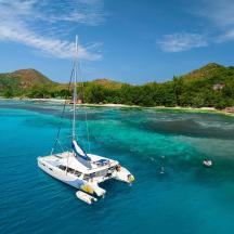 a white sail boat in the water near a beach