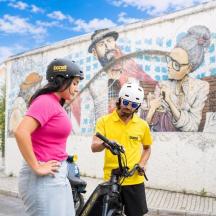 a woman standing next to a man on a bike in front of a mural