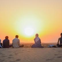 en gruppe mennesker som sitter på stranden og ser på solnedgangen