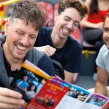 three men laughing while looking at a magazine