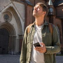 vyras stovi priešais pastatą ir laiko mobilųjį telefoną