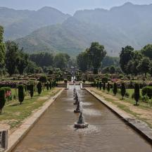 a garden with a fountain and trees and mountains in the background