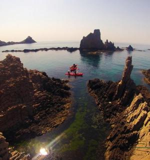two people in a kayak in the water near rocks