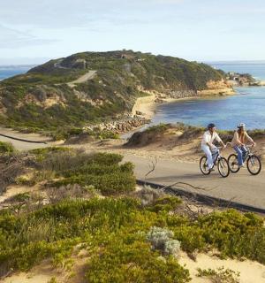 dva lidé jedoucí na kolech po silnici u oceánu