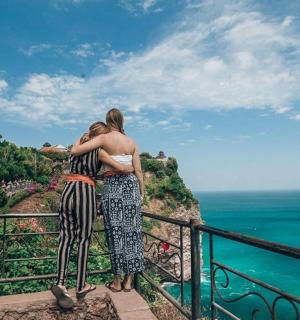 two women standing on a ledge looking at the ocean