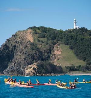 一群人在水中乘船，旁边有一座灯塔