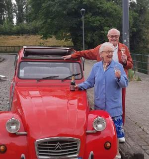 two older men standing next to a red car