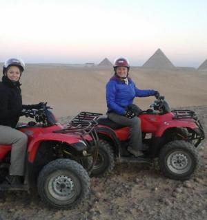 two people on atvs in the desert with pyramids in the background